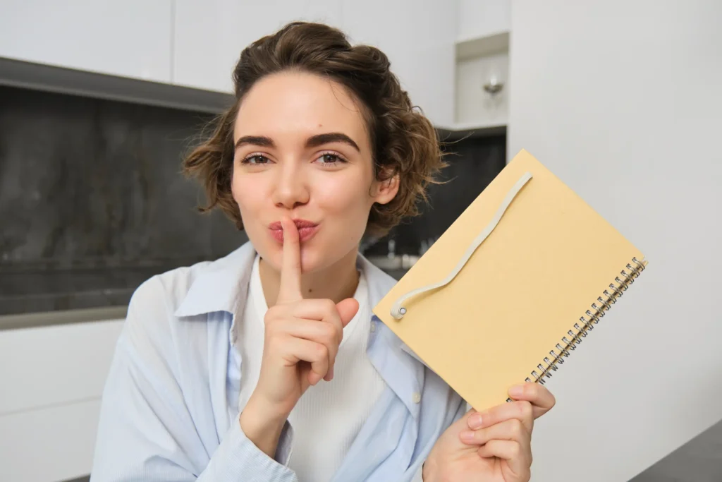 A young woman holding a notebook, making a “shush” gesture to hint at secret methods for Polish Leaving Cert success.