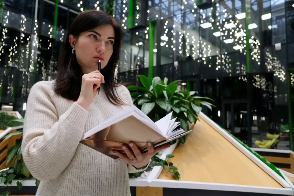 A student holding a notebook, thoughtfully planning her Leaving Cert preparation with polishonline.ie in a modern indoor setting.